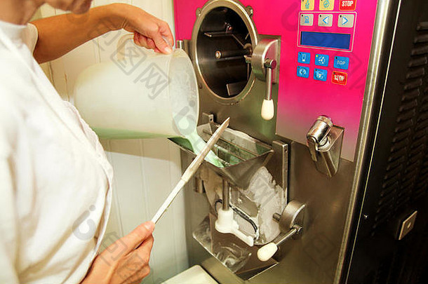 冰淇淋厂的女厨师正在将混合的基本配料、牛奶、薄荷口味的混合物倒入冰淇淋机中。