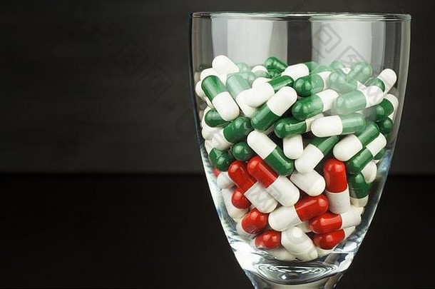 一杯维生素药丸。黑色背景玻璃容器中的药物。运动员营养补充剂。饮食观念。