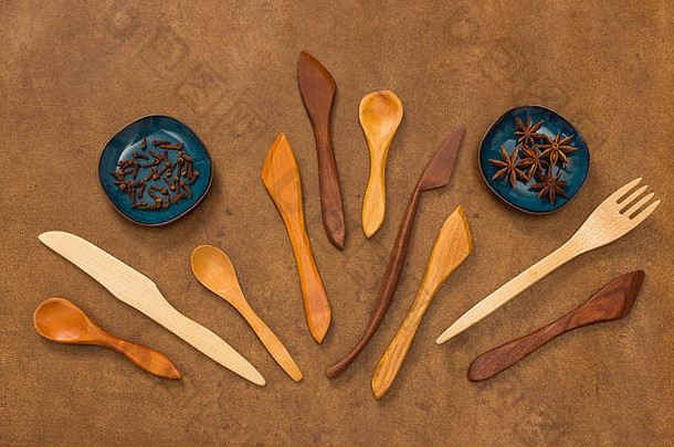 棕色皮革背景上手工制作的木制器皿和香料。叉子、勺子和刀。丁香和茴香。