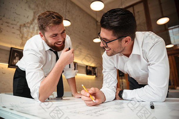 两个年轻快乐的商人站在桌子边，手里拿着<strong>一张图</strong>，正在做<strong>一</strong>份商业计划书