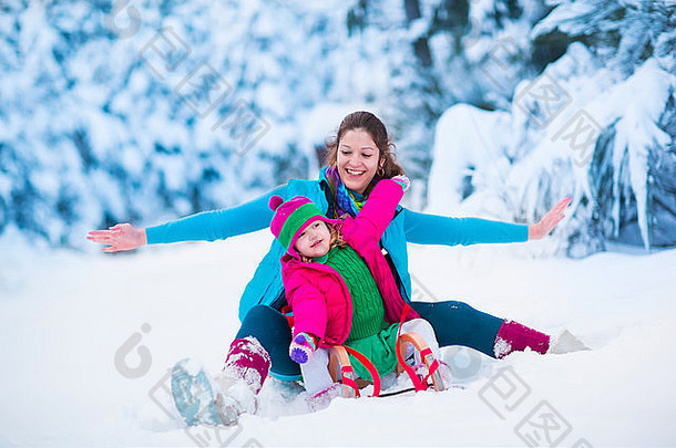 年轻的母亲和小女孩正在玩雪橇。儿童雪橇。蹒跚学步的孩子骑着雪橇。孩子们在户外雪中玩耍。