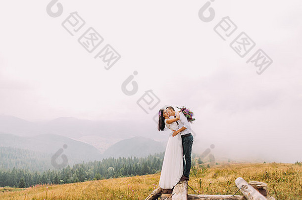 美丽的新婚夫妇在木桥上接吻。山上的雾天