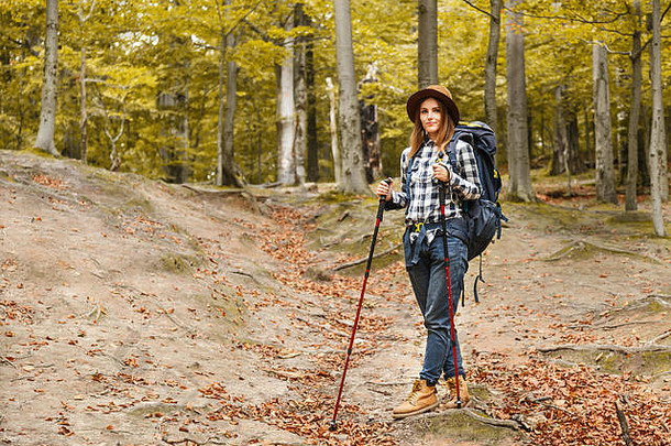 年轻的微笑着的女士戴着帽子在山上徒步旅行，并有一个放松的休息，她留下来，拿着登山杖，旅行