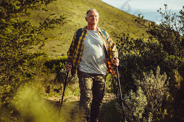在丘陵地带徒步旅行的<strong>冒险者</strong>。一位老人拿着登山杖在山路上行走。