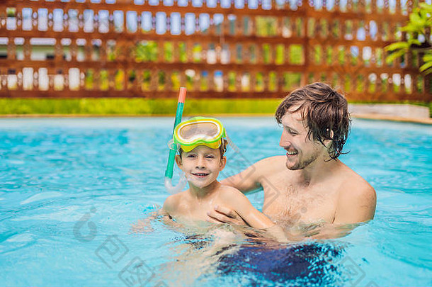 戴泳镜的爸爸和儿子在游泳池里玩得很开心