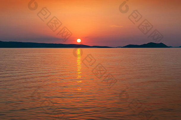 太阳落在克罗地亚海岸附近海面上的山脉上。橙色和红色的风景