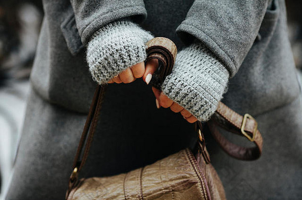 一个穿着外套和针织手套的女孩拿着一个皮包。手的特写。女人期待，紧张。压缩的手，美丽的指甲