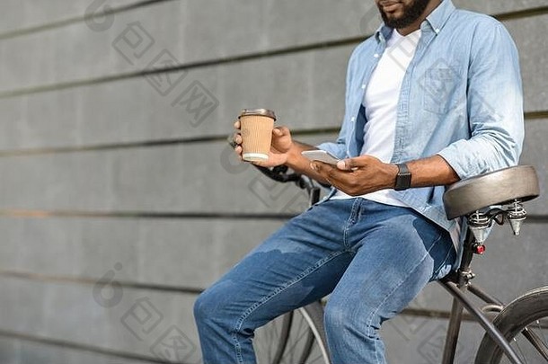 坐在自行车上，拿着智能手机和外卖咖啡的黑人千禧一代