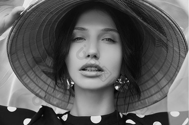 一位身穿时尚连衣裙、头戴中国草帽、肤色黝黑的漂亮女人在花园里摆姿势的肖像