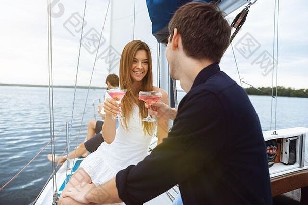 一对幸福微笑的夫妇在户外的船上聚会上喝着伏特加鸡尾酒，欢快而快乐。年轻人享受海游、青春和暑假的乐趣。酒精，假期，休息，爱。