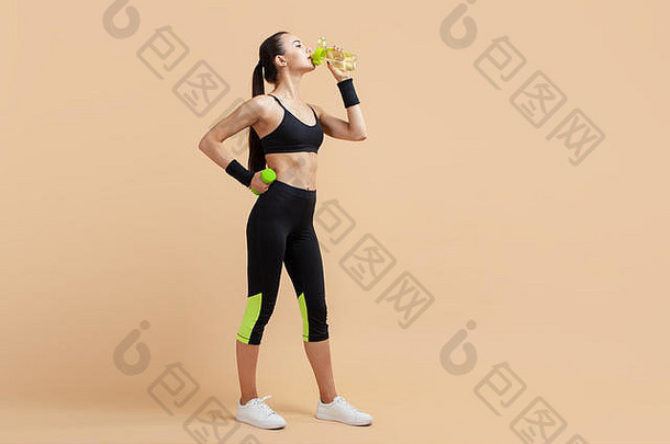 一个迷人的浅黑色运动女孩，可爱，穿着紧身运动服，站得高高的，在锻炼后从瓶子里喝水。