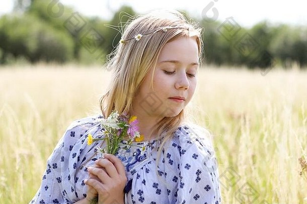 一个年轻漂亮的嬉皮女孩，金色头发上戴着一条雏菊链，在夏日牧场的阳光下手持一束野花。
