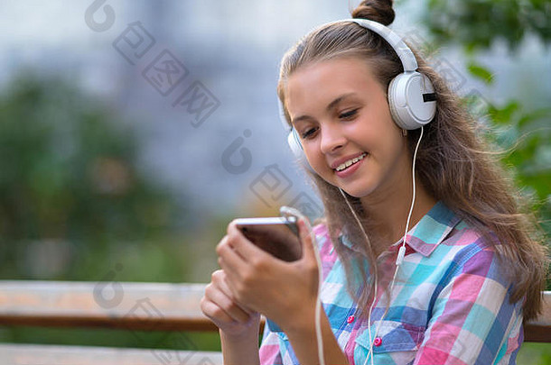 坐在户外用立体声耳机听音乐时，微笑着的年轻女子正在手机上选择新的配乐