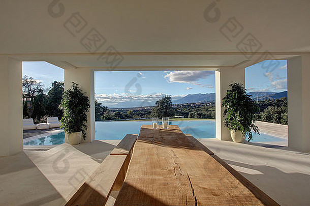 大型现代西班牙别墅游泳池旁阳台上的乡村木桌和长凳