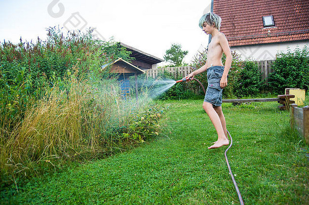 一个蓝发少年用软管浇灌草坪