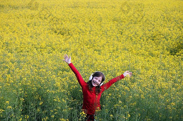 快乐的小女孩举手在黄色的田野上听音乐