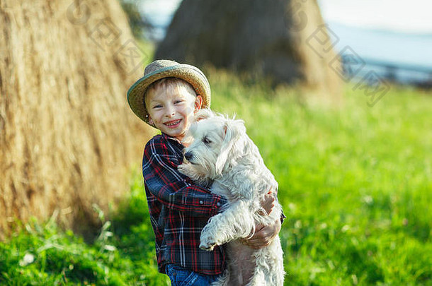 男孩拥抱着和狗站在一起，户外半幅肖像，草垛背景。年轻人和动物在绿色的乡村里欢欣鼓舞。好朋友