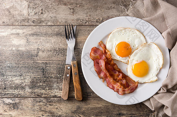 早餐在木桌上煎鸡蛋和熏肉。顶视图。版面