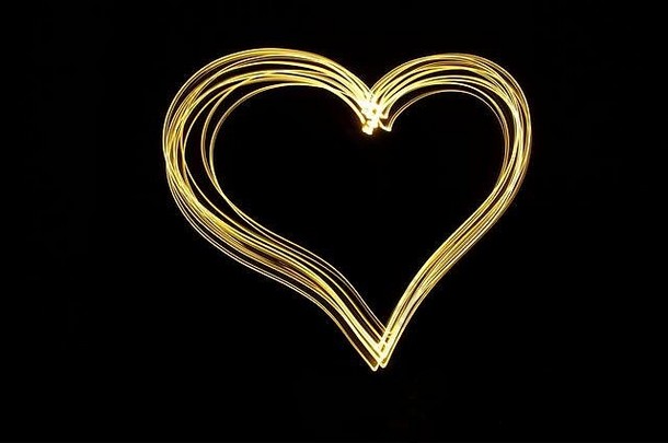 一张心形轮廓的光绘照片，在黑色背景下呈现明亮的霓虹金色。长曝光摄影。爱情，浪漫。
