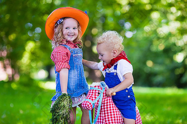 小男孩和小女孩装扮成牛仔和牛仔女孩，在公园里玩玩具摇马。孩子们在户外玩耍
