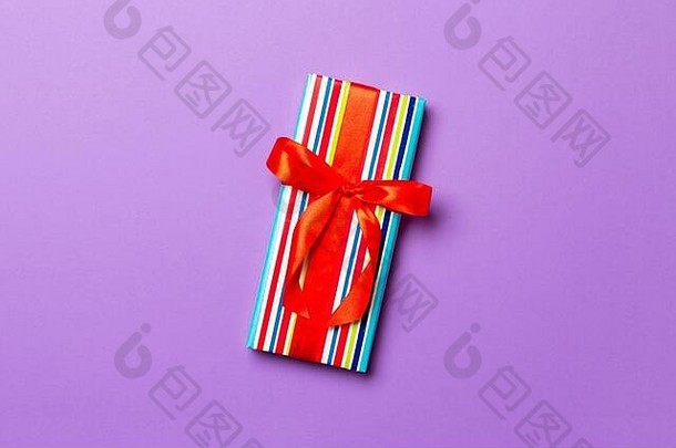 用紫色背景上的红丝带用纸包好的圣诞节或其他节日手工礼品。礼品盒，彩台礼品装饰，t