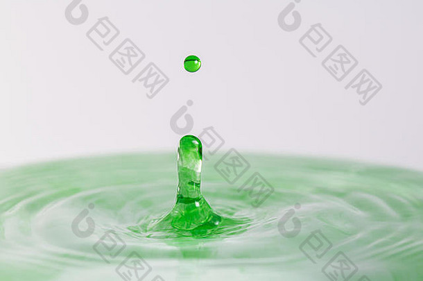 一个绿色水滴在浅色白灰色背景下溅入水中的特写微距摄影