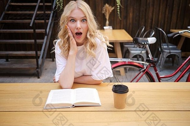 有吸引力的震惊了金发碧眼的女孩惊奇地相机书咖啡院子里城市咖啡馆