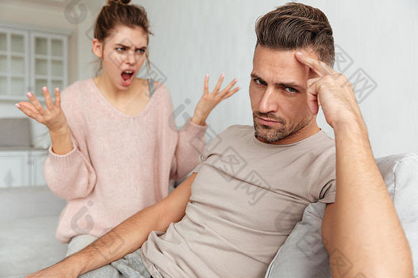 一个心怀不满的男人和他的女朋友坐在沙发上，在家里和他一起尖叫和争吵