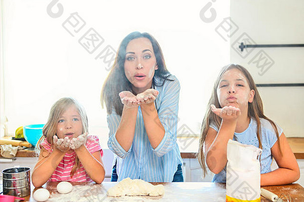 快乐的年轻母亲和女儿在厨房里用筛子把面粉倒进面团里玩得很开心