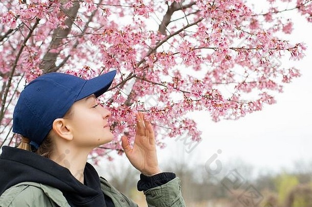 春天的开始。美丽的女人欣赏大自然盛开的树木。春季过敏概念