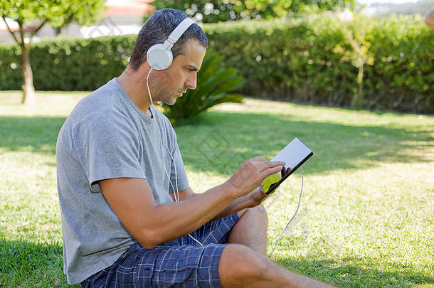 年轻人在公园、户外的沙发上用平板电脑放松，戴着耳机听音乐