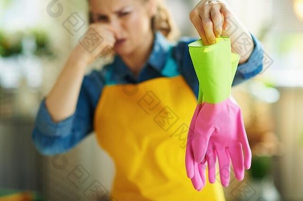 在阳光明媚的日子里，一个穿着橙色围裙和粉色橡胶手套的恶心女人在客厅里拿着臭手套。