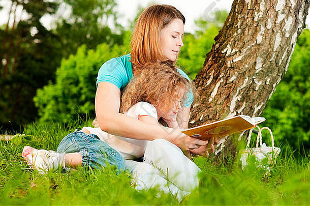 年轻的母亲坐在<strong>树下</strong>的草地上，给躺在母亲膝上的小女儿<strong>读书</strong>