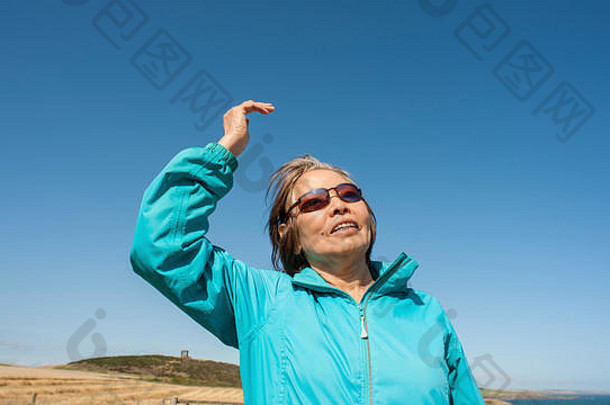 成熟的亚洲女士抬起右手，看着远处的蓝天，表情有待解读。