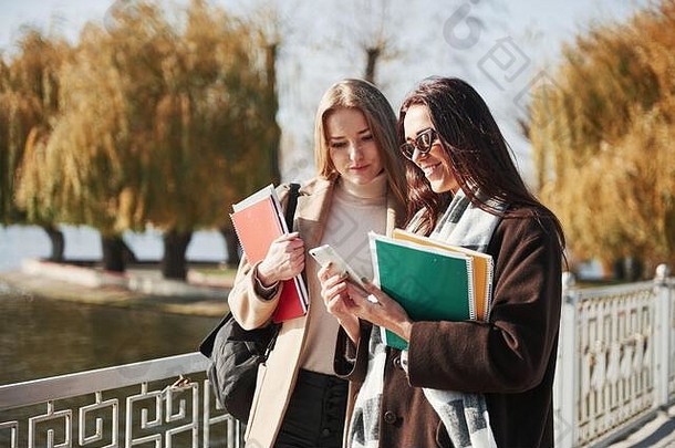 看看这些考试成绩。两名女学生拿着笔记本在公园的桥上散步