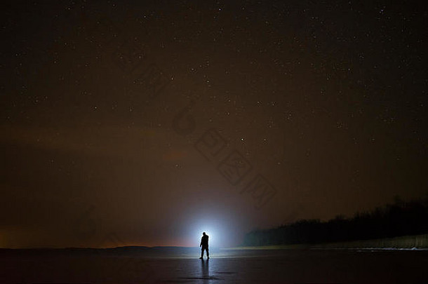 人在夜间用手电筒照明。站在冰湖上。