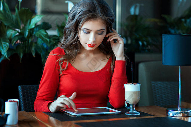 咖啡馆里的一个女孩坐在桌子旁，为电脑平板电脑工作。