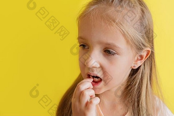 这孩子掉了第一颗乳牙。改变牙齿观念。可爱的小女孩，金色头发，黄色背景，有复印空间。