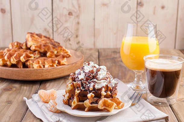 早餐甜甜的比利时华夫饼，用白奶油和巧克力酱装饰。咖啡黑、橙汁、水果、香蕉和葡萄的咖啡杯，棕色木质背景。为…腾出空间。