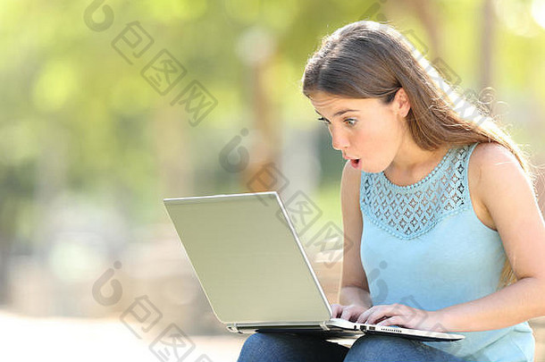 坐在公园里查看笔记本电脑在线内容的惊讶女人