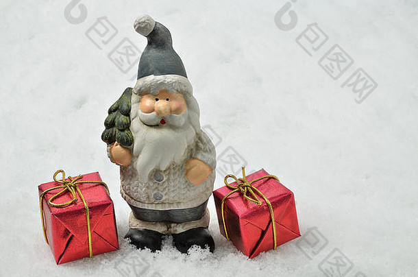 圣诞老人的陶瓷雕像，灰色衣服，圣诞树和雪地背景上的两个红色包裹，水平