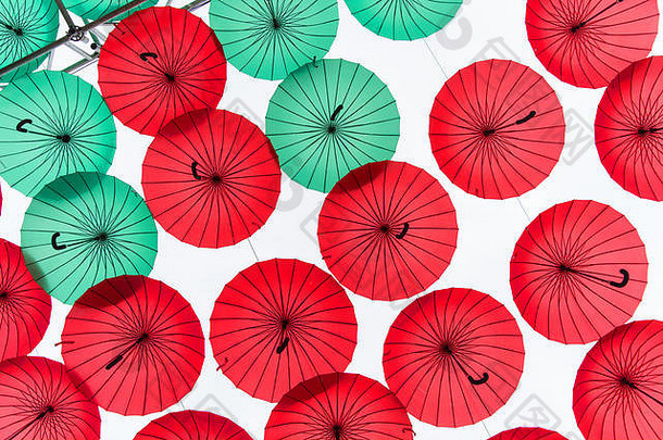 美丽的彩色雨伞或阳伞，红绿相间的檐篷和弯曲的把手挂在户外的白色天空背景上