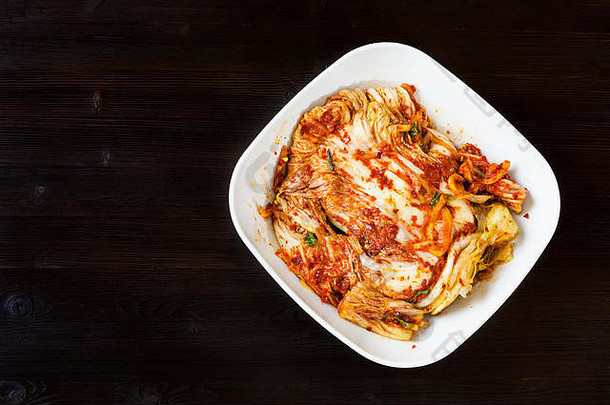 韩国料理-深棕色木桌上白色碗中的泡菜开胃品（辛辣纳帕卷心菜）俯视图，带有文字空间