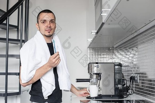 一个年轻人早上要去上班。在咖啡机旁刷牙，等待一杯咖啡。
