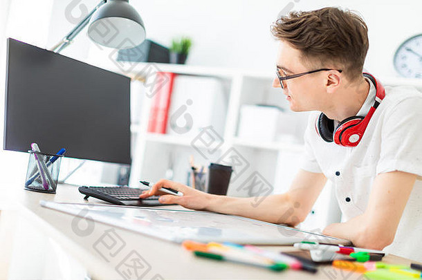 年轻的男人。眼镜站电脑桌子上年轻的男人。作品电脑磁董事会脖子盖伊耳机挂