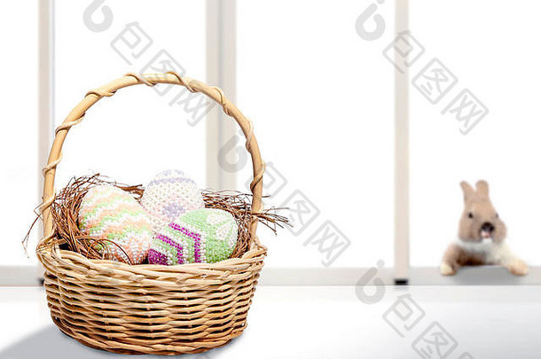 五颜六色的复活节彩蛋放在桌子上的木篮子里，小兔子放在窗户玻璃的背景上。复活节快乐