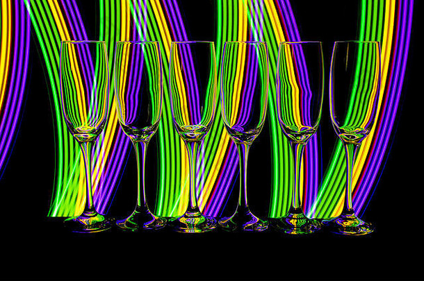一排六个空香槟酒杯/长笛，在黑色背景上相互隔离，后面有彩色霓虹灯<strong>条</strong>纹的光画