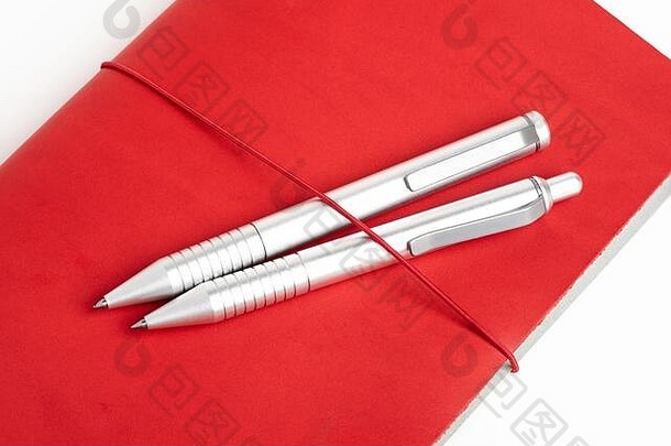 一种有红色皮革封面和松紧带的日记本，用来固定两支金属圆珠笔。
