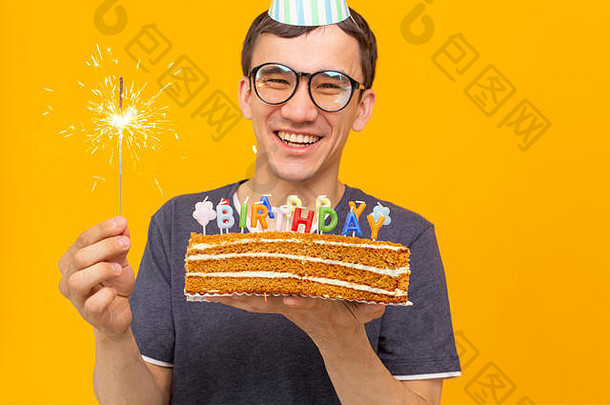 一个戴着眼镜、戴着纸礼帽、手持蛋糕、站在黄色背景上的疯狂快乐的年轻人，生日快乐。<strong>周年庆</strong>祝