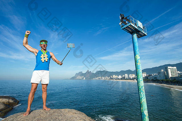 在里约热内卢伊帕内马海滩的阿波多尔，一名金牌运动员拿着手机在<strong>自拍杆</strong>上摆姿势拍照